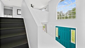 A staircase leading to a second floor with a teal door and a large arched window. - Coastal Retreat - Roomy, Relaxing Heated Pool (Palm Coast)