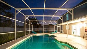 An outdoor swimming pool with a covered area, lounge chairs, and a building with a door and windows. - Coastal Retreat - Roomy, Relaxing Heated Pool (Palm Coast)