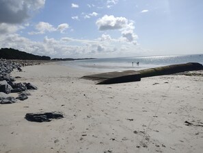 Une plage de sable avec de gros rochers sur la gauche, une barrière en béton au centre et un ciel dégagé avec quelques nuages.