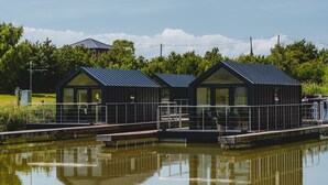 A modern building with a metal roof and large windows, situated next to a calm body of water. - Whimbrel (Chester)