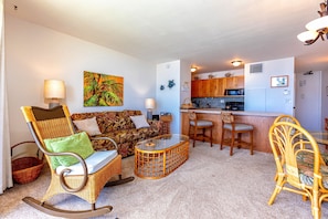 A living room with a sofa, chairs, a glass coffee table, and a kitchen area with wooden cabinets and a microwave. - Sugar Beach Resort #227 1 Bedroom Condo by RedAwning (Kihei)