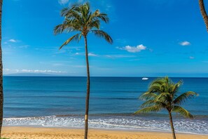 A beach with palm trees and a boat in the distance. - Sugar Beach Resort #227 1 Bedroom Condo by RedAwning (Kihei)