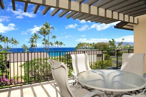 A balcony with a table and chairs overlooking a beach with palm trees and the ocean. - Wailea Elua, #1508 2 Bedroom Condo by RedAwning (Kihei)