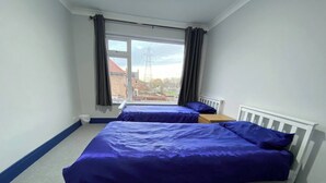 A bedroom with two beds, a window with curtains, and a view of buildings outside. - 3 Room Apartment - Twins-double (King's Lynn)