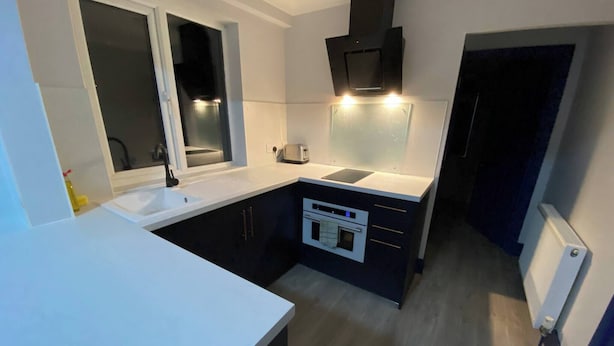 A compact kitchen with a window, built-in oven, and a black range hood. - 3 Room Apartment - Twins-double (King's Lynn)