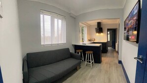 A compact living space with a sofa, a kitchenette, and a bar area. - 3 Room Apartment - Twins-double (King's Lynn)