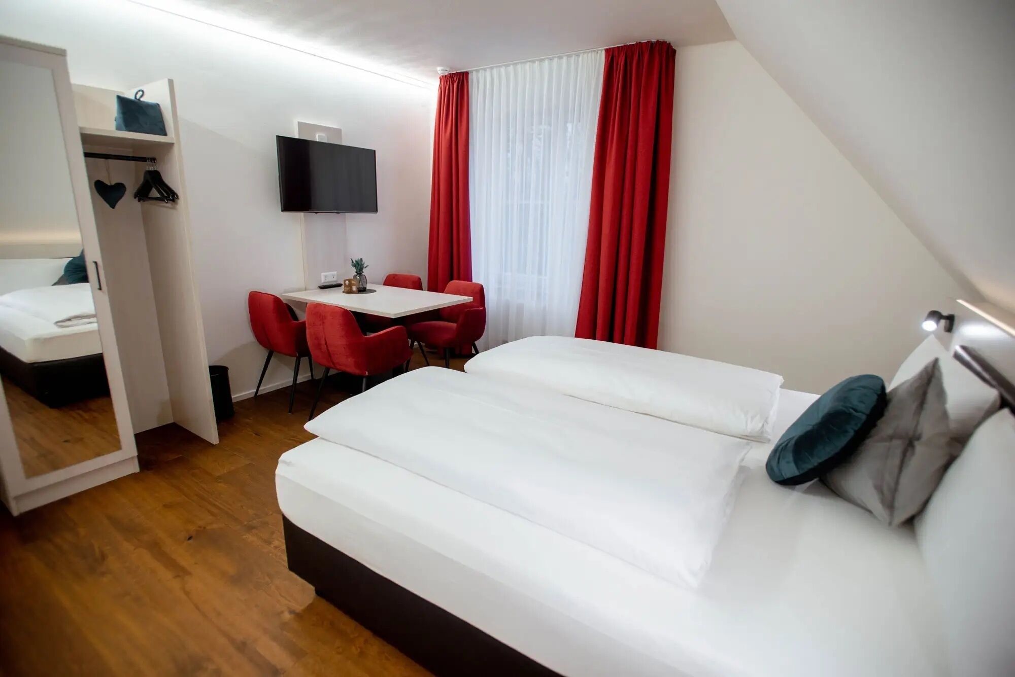 Ein Hotelzimmer mit einem Bett, einem Schreibtisch mit Stuhl, einem Fernseher und einem Kleiderschrank.