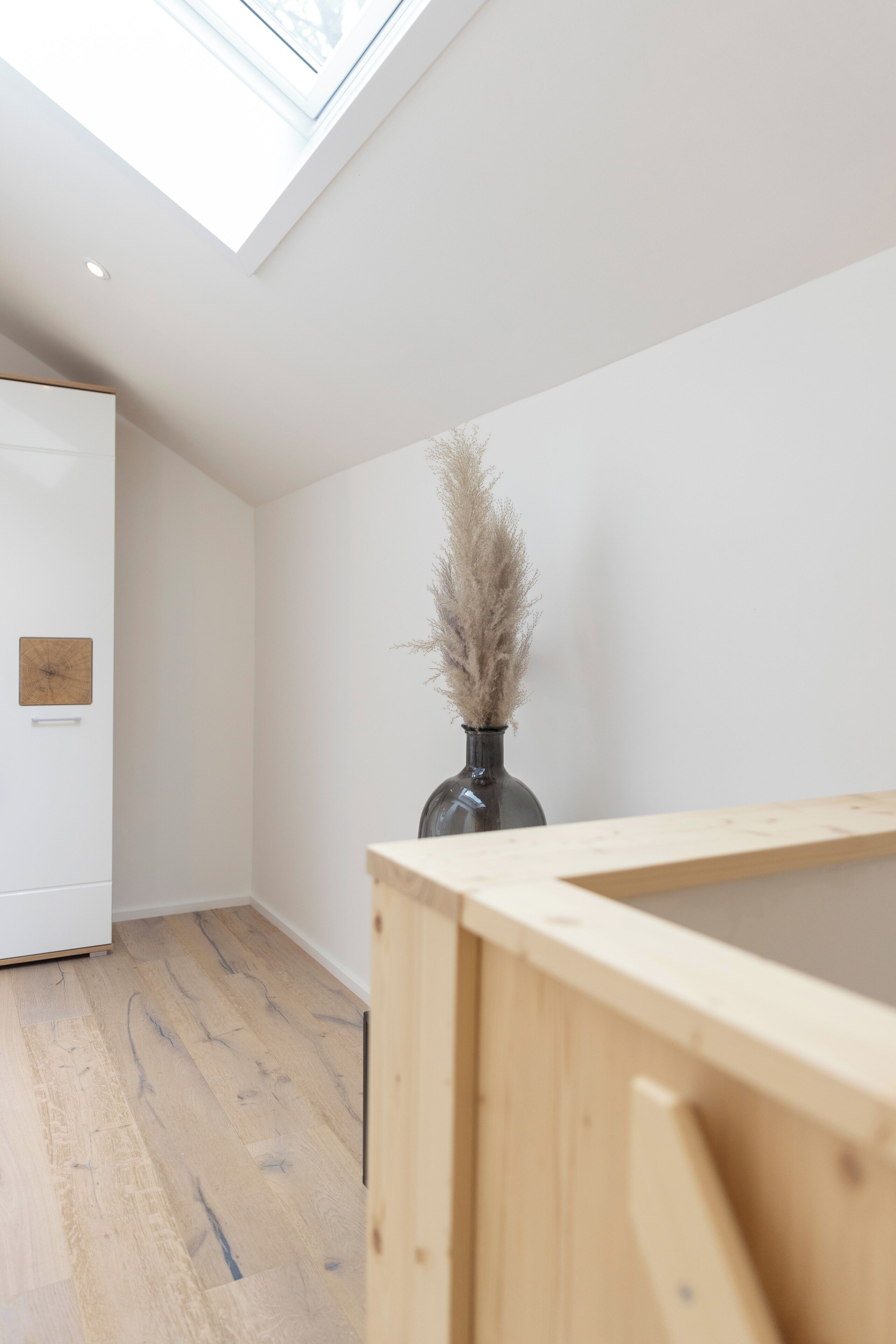 A modern interior with a skylight, a wooden floor, and a vase with dried plants.