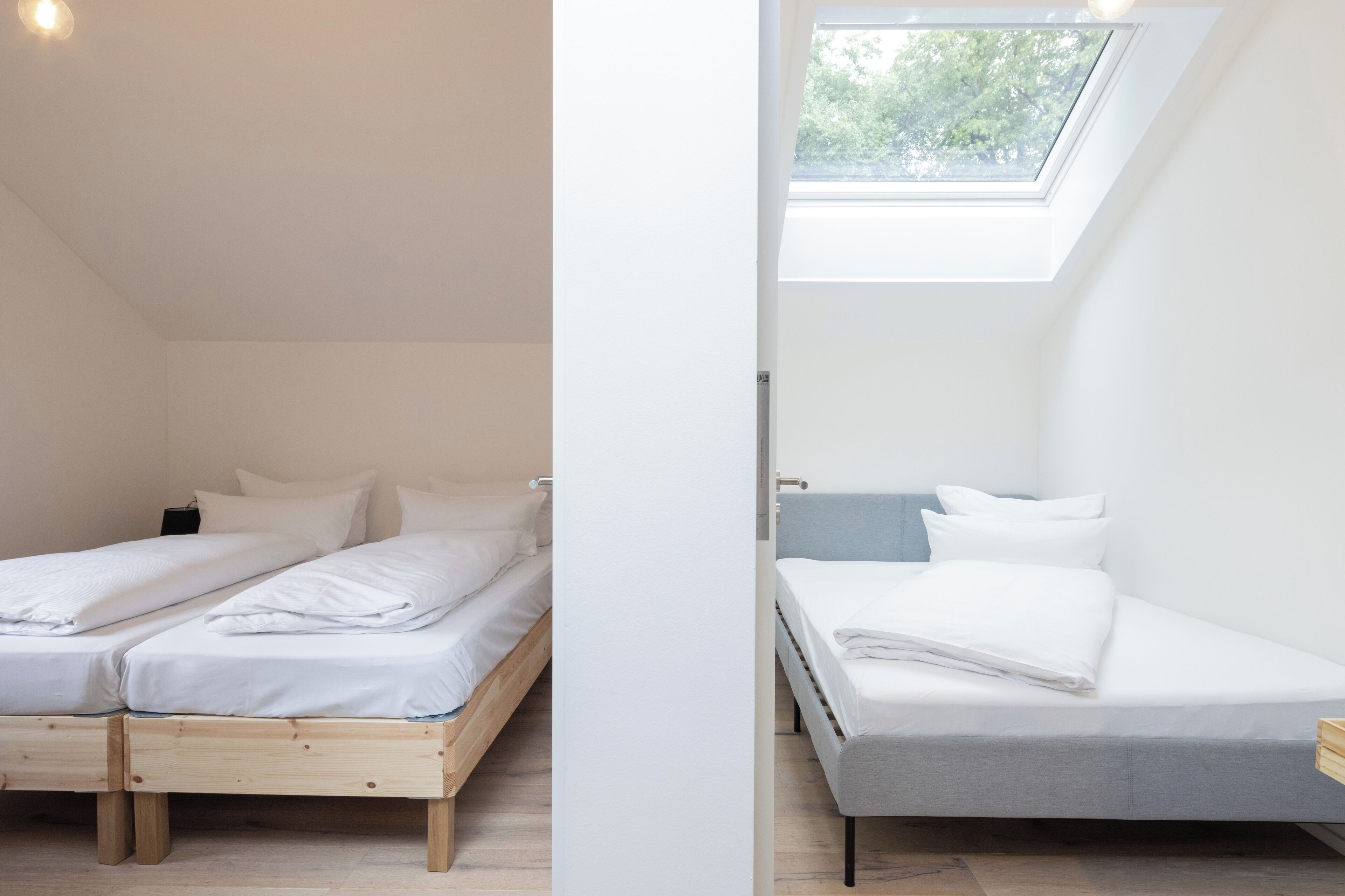 A room with two wooden beds, a skylight, and a white wall.