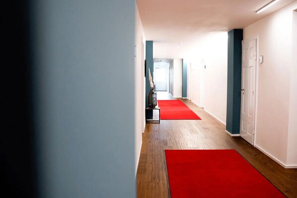 Un pasillo con piso de madera y alfombras rojas, que conduce a una puerta al final.