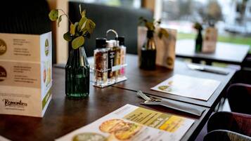 Un tavolo da ristorante con un menu, una bottiglia verde e una pianta, e svariati condimenti.