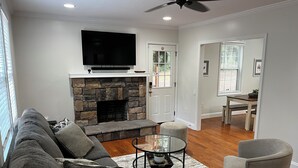 A living room with a stone fireplace, a flat-screen TV, a sofa, a coffee table, and a dining area with a table and chairs. - 5 Points House - Great Location - 3Br2Ba - Early Check-In (Athens)