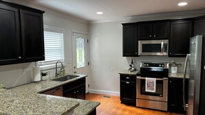 A modern kitchen with dark cabinets, granite countertops, stainless steel appliances, and a wooden floor. - 5 Points House - Great Location - 3Br2Ba - Early Check-In (Athens)