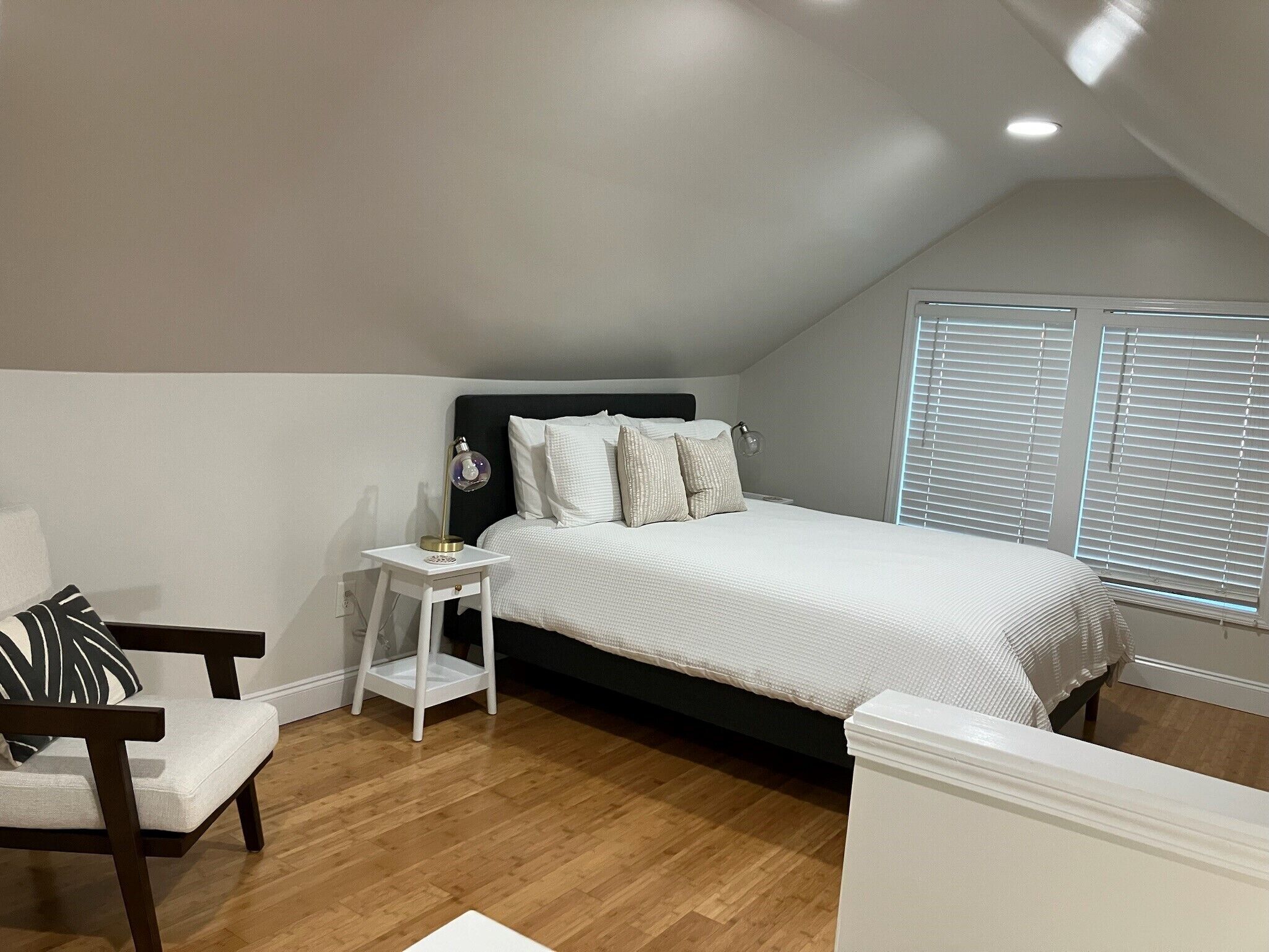 Une chambre à coucher comprenant un lit, une table de chevet, une chaise et une fenêtre avec des stores.