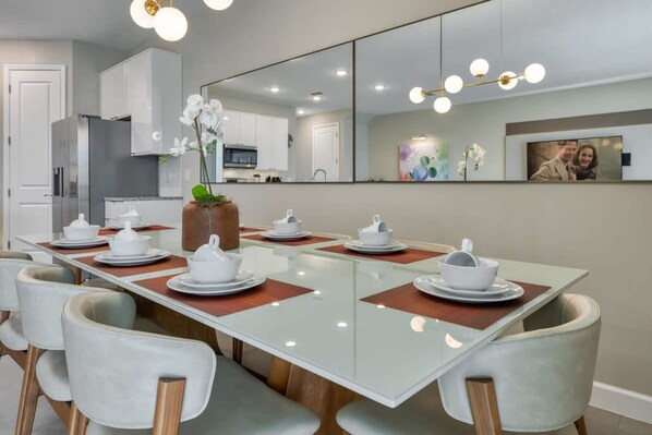 A modern dining area with a long table set for six, surrounded by cushioned chairs.