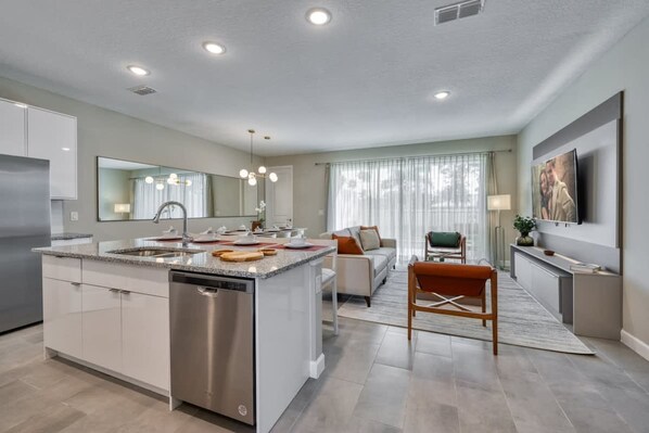 A modern kitchen with a central island, built-in appliances, and a dining area with a sofa and chairs. - Modern Spacious Home With Themed Bedroom and Private Pool (Kissimmee)