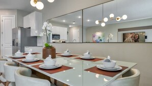 A modern dining area with a long table set for six, surrounded by cushioned chairs. - Luxury new Home Close to the Parks (Kissimmee)