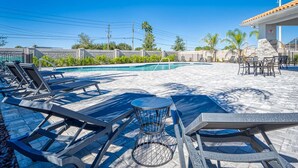 A pool area with lounge chairs, a small table, and a covered seating area. - Luxury new Home Close to the Parks (Kissimmee)