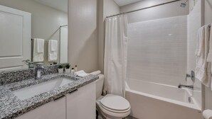 A bathroom with a granite countertop sink, a toilet, a bathtub with a shower curtain, and a mirror. - Luxury new Home Close to the Parks (Kissimmee)