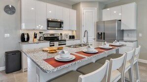A modern kitchen with white cabinets, stainless steel appliances, granite countertops, and a built-in island with seating. - Spacious and Modern Home for 9 Guests (Kissimmee)