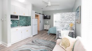 Un espacio habitable compacto con kitchenette, una cama, un televisor y un ventilador de techo.