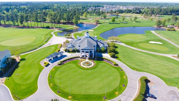 Un campo de golf con club house, un estanque y césped bien cuidado.