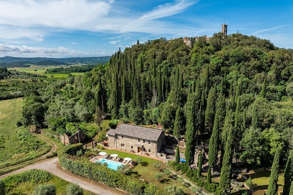 A stone villa with a swimming pool, surrounded by lush greenery and a hilltop view.