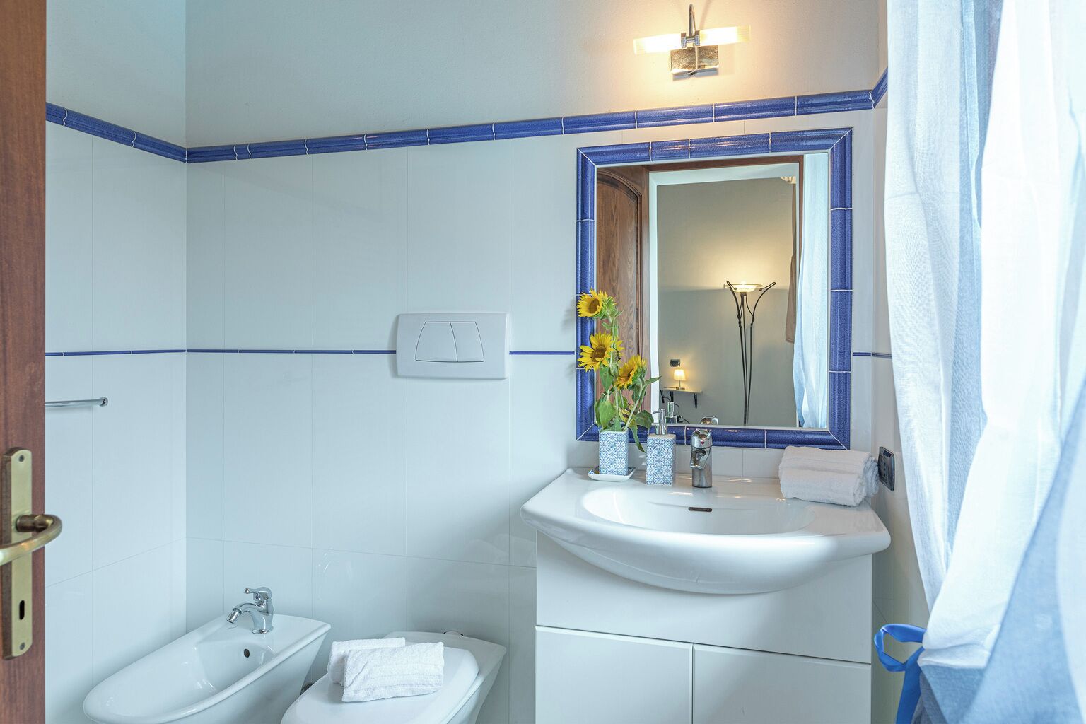 A bathroom with a sink, mirror, and bidet. There is a towel on the bidet and a vase with flowers on the sink.