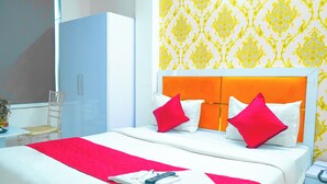 Una cama bien hecha con una decoración rojo y blanco, una mesita de noche con un teléfono, y una silla en una habitación con papel tapiz estampado y un armario.