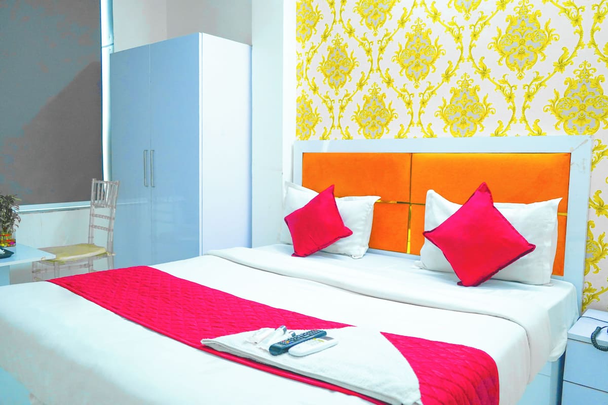 Una cama bien hecha con una decoración rojo y blanco, una mesita de noche con un teléfono, y una silla en una habitación con papel tapiz estampado y un armario.