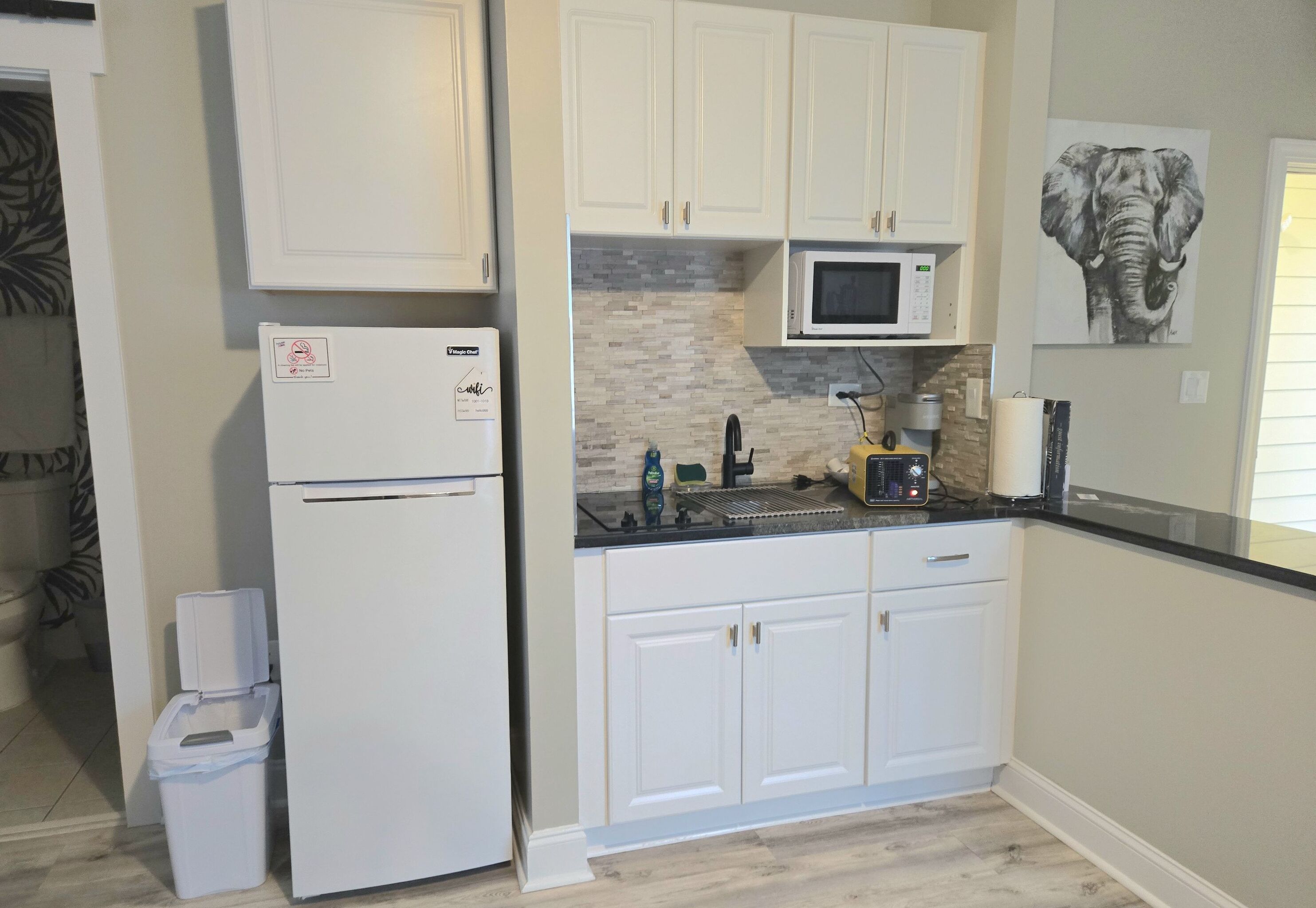 A kitchen with white cabinets, a microwave, and a trash bin.