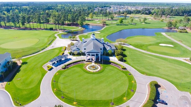 Un campo da golf con un club house, uno stagno e un prato curato.