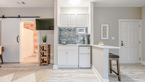 A modern kitchen with white cabinets, a tiled backsplash, and a small island with stools. - Mini Oasis Studio 10 Min to All Myrtle Beach (Myrtle Beach)