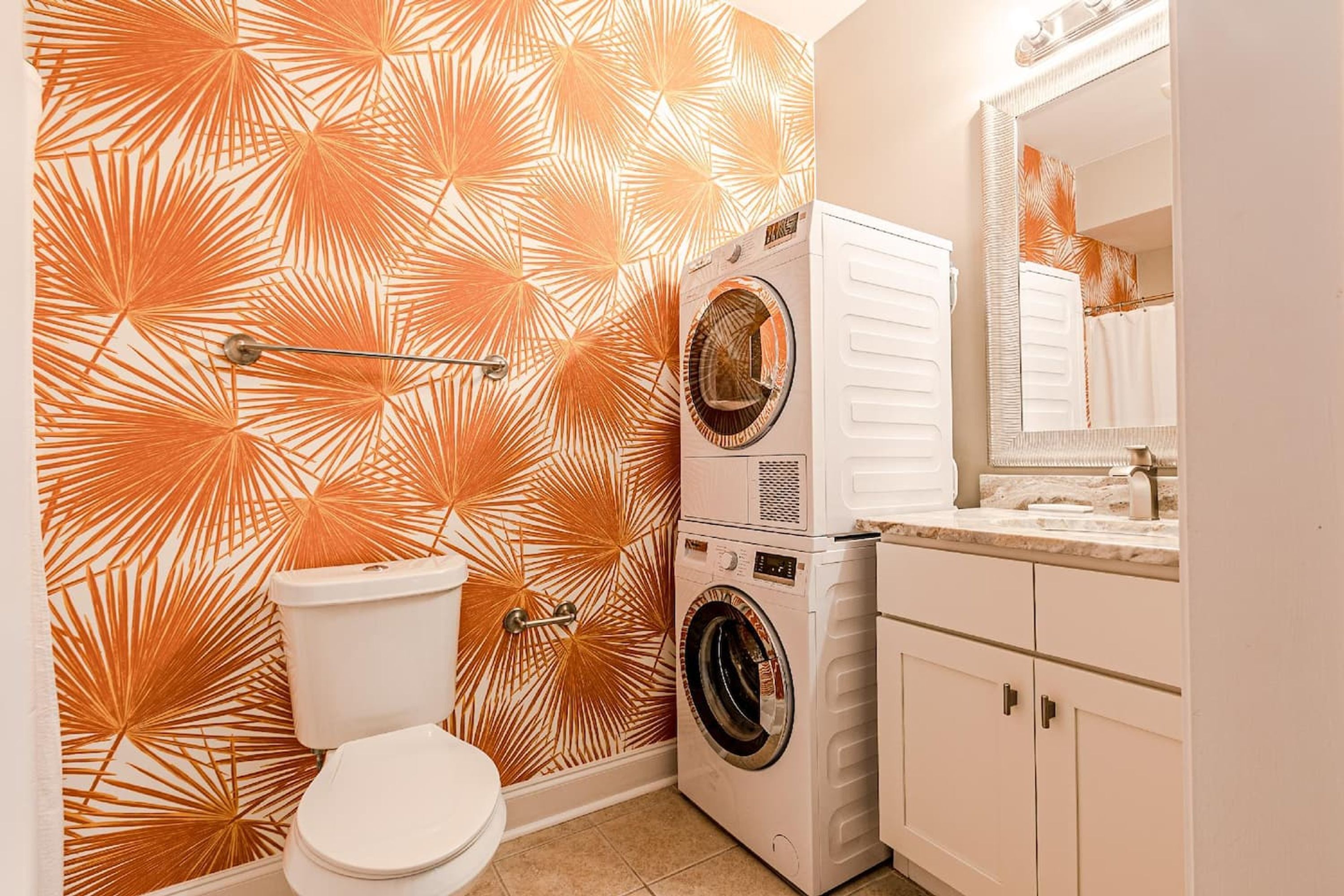 Een badkamer met een behang, een toilet, een wasmachine en een spiegel.