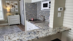 Cozinha com bancada de granito, micro-ondas, chaleira e pia.