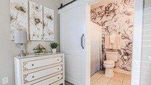 Casa de banho com papel de parede floral, sanita e área de duche.