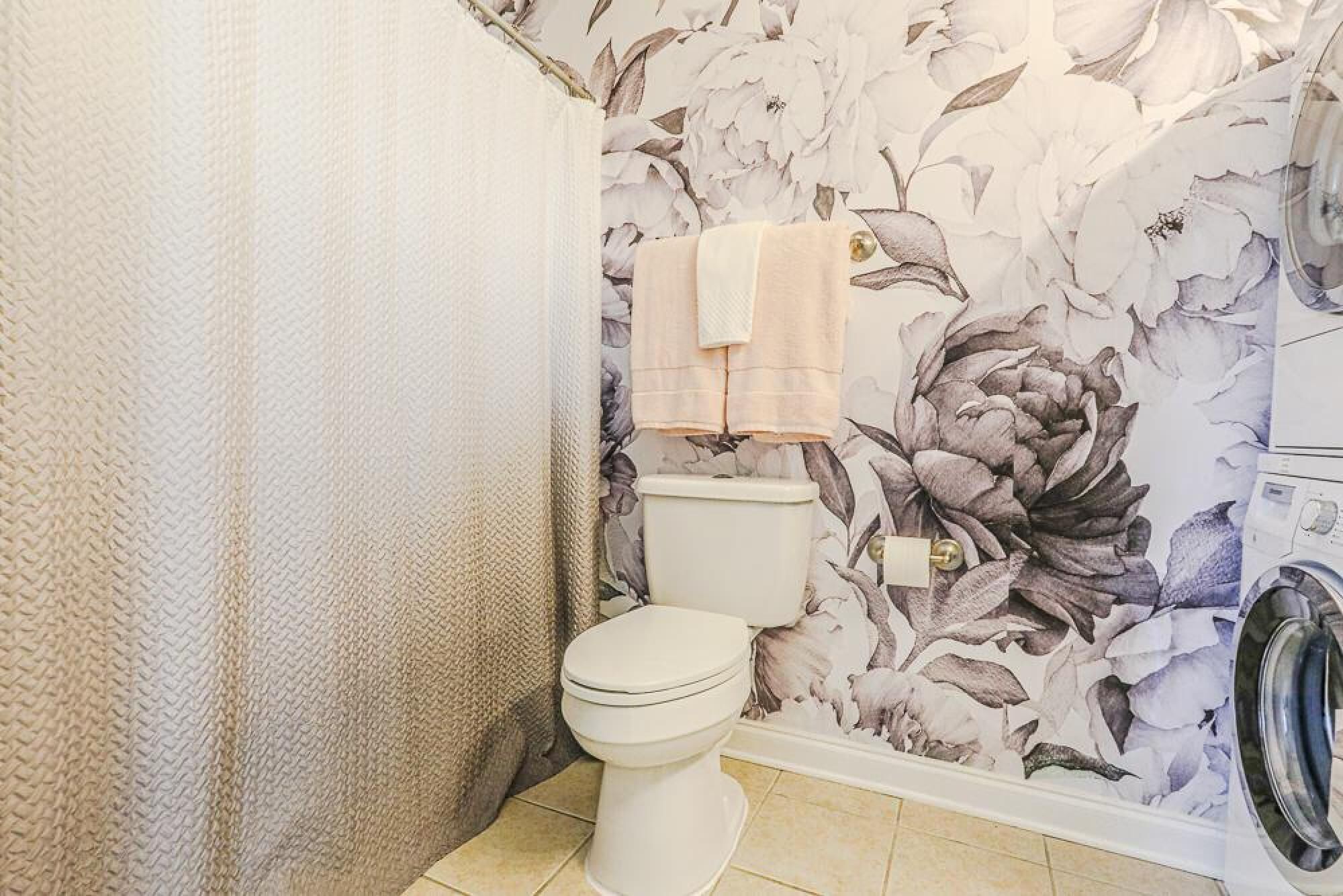 A bathroom with a toilet, a shower curtain, and a floral wallpaper.