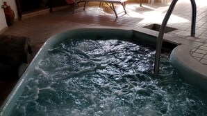 Banyera d'hidromassatge amb interior de rajola, una porta de fusta i vistes a una zona d'estar exterior amb taula i cadires.