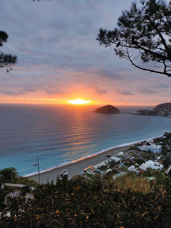 A coastal sunset view with a beach, a small island, and a residential area with buildings.