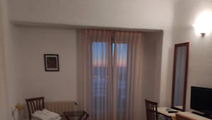 Habitació d'hotel amb dos llits, un escriptori, una cadira, un televisor i una finestra amb cortines.
