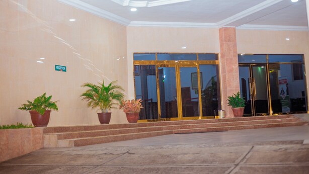 A hotel entrance with a reception desk, potted plants, and a glass door. - Eden Hotels Ltd (Eket)