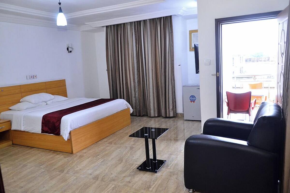 A hotel room with a bed, a small table, a chair, and a view of the outside.