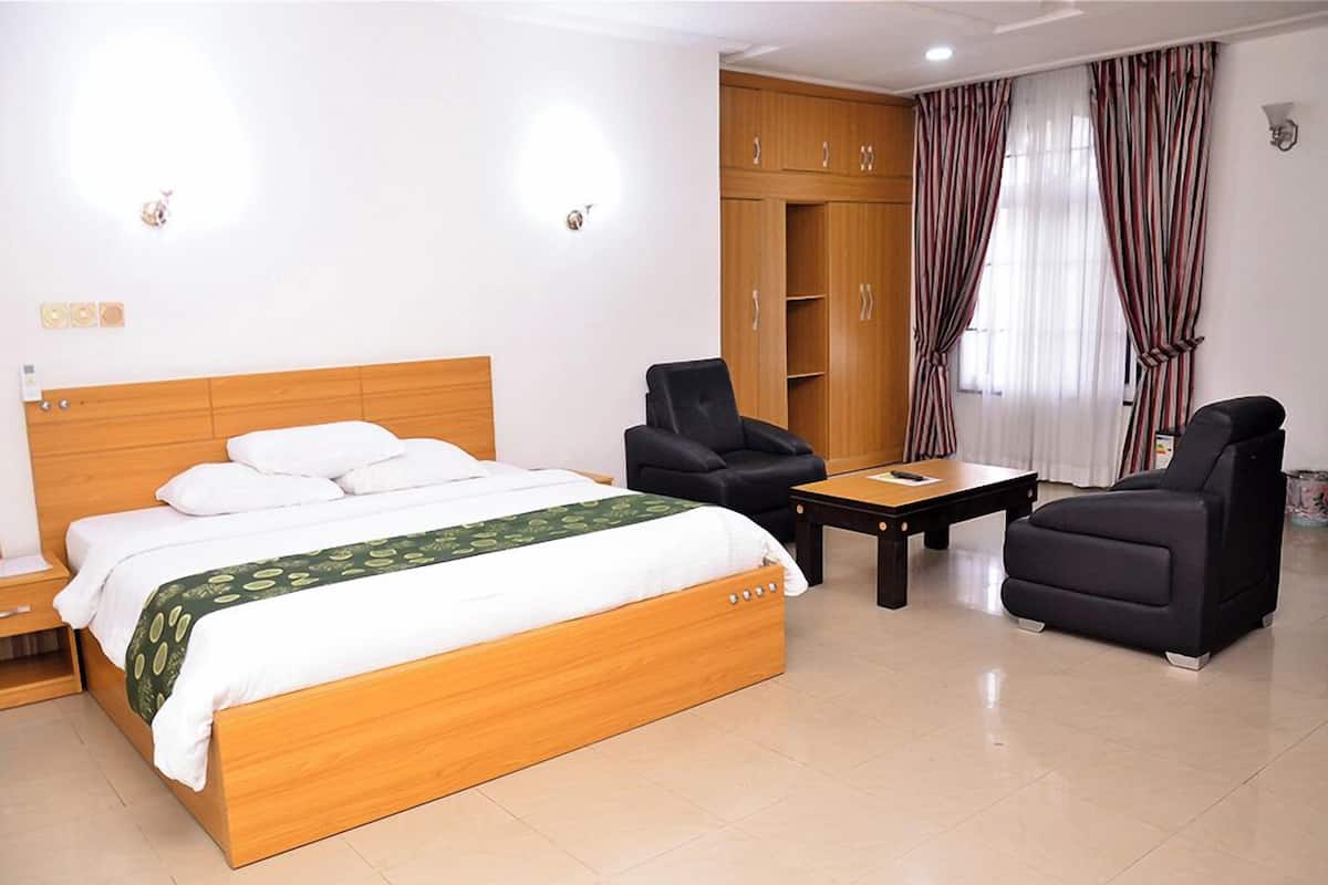 A hotel room with a wooden bed, two black armchairs, a small table, and a wardrobe.