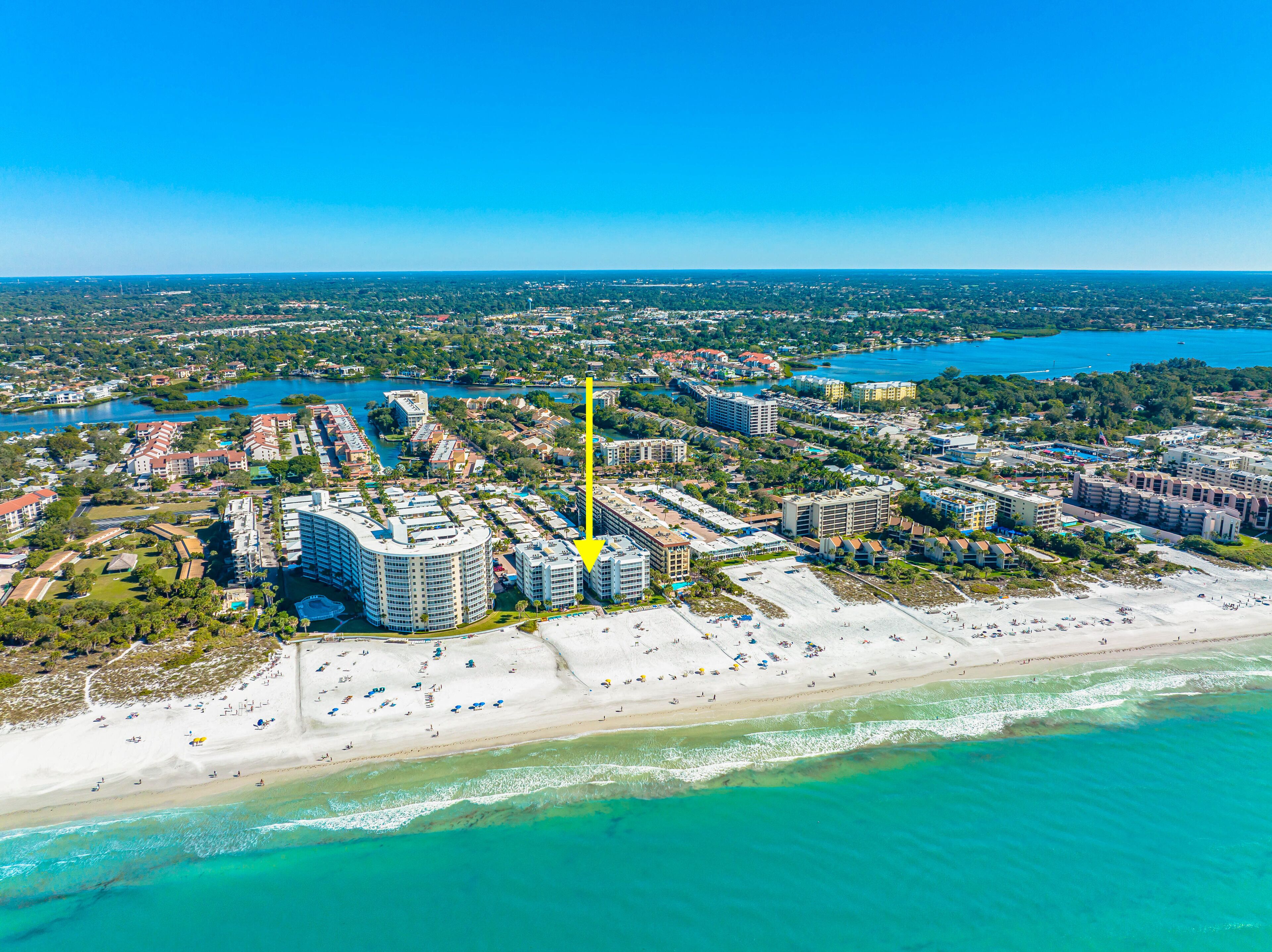 An aerial view of a coastal city with a prominent hotel complex, beachfront, and surrounding urban area.