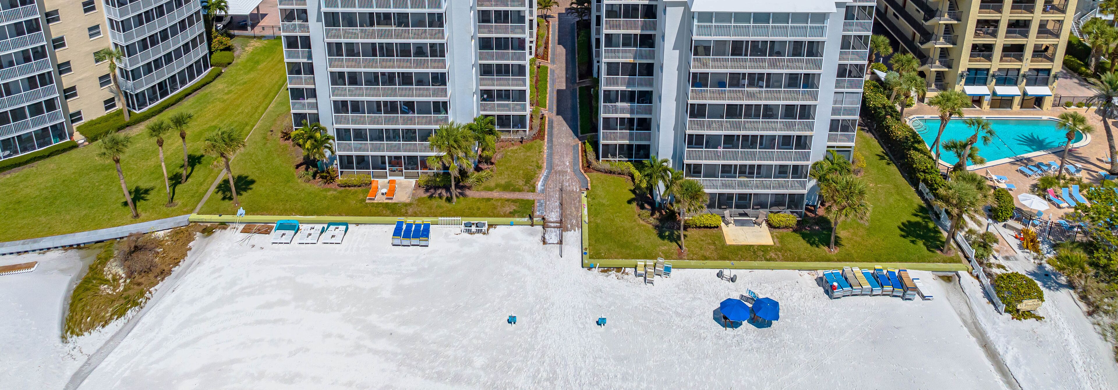 An aerial view of a modern hotel complex with multiple high-rise buildings, a swimming pool, and a beach area with sun loungers.