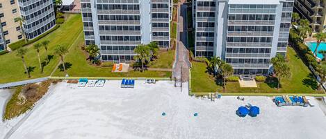 An aerial view of a modern hotel complex with multiple high-rise buildings, a swimming pool, and a beach area with sun loungers.