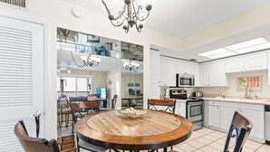 A modern kitchen with white cabinets, a round wooden dining table, and a chandelier. - 2 Bedroom Condo at Crescent Arms Steps from the Beach! (Sarasota)