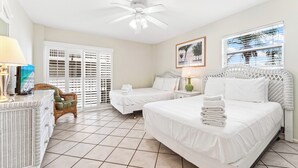 A hotel room with two beds, a ceiling fan, a wicker chair, and a large window with blinds. - 2 Bedroom Condo at Crescent Arms Steps from the Beach! (Sarasota)