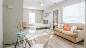 A modern living room with a glass dining table, a beige sofa, and a ceiling fan. - My Vitamin Sea Quaint Studio Myrtle Beach SC (Myrtle Beach)