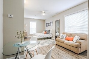 A modern living room with a glass dining table, a beige sofa, and a ceiling fan. - My Vitamin Sea Quaint Studio Myrtle Beach SC (Myrtle Beach)